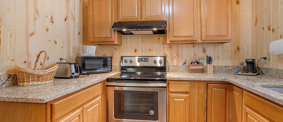 A kitchenette with granite countertop featuring a range, and kitchen appliances with utensils and flatware next to stove. 