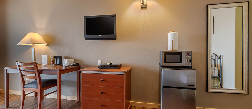 A television on the wall above a dresser is flanked by a small sitting area and a microwave atop a mini-fridge. 