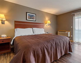 A bed centered between two light fixtures high upon the wall, with see through curtains on exit door.