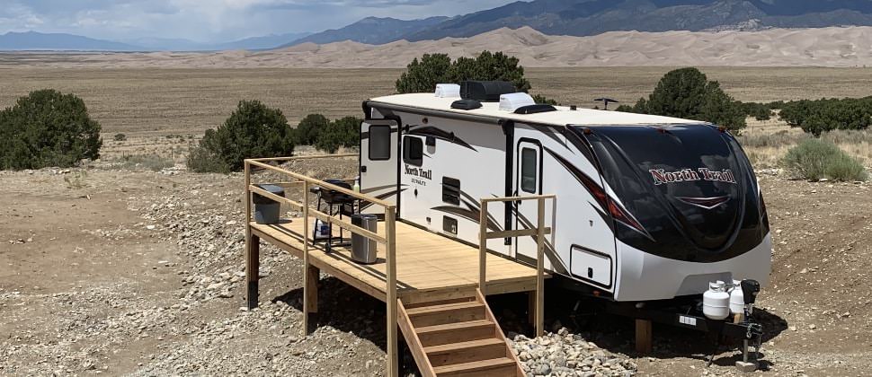 Camper and wooden deck with sand dunes and mountains in background
