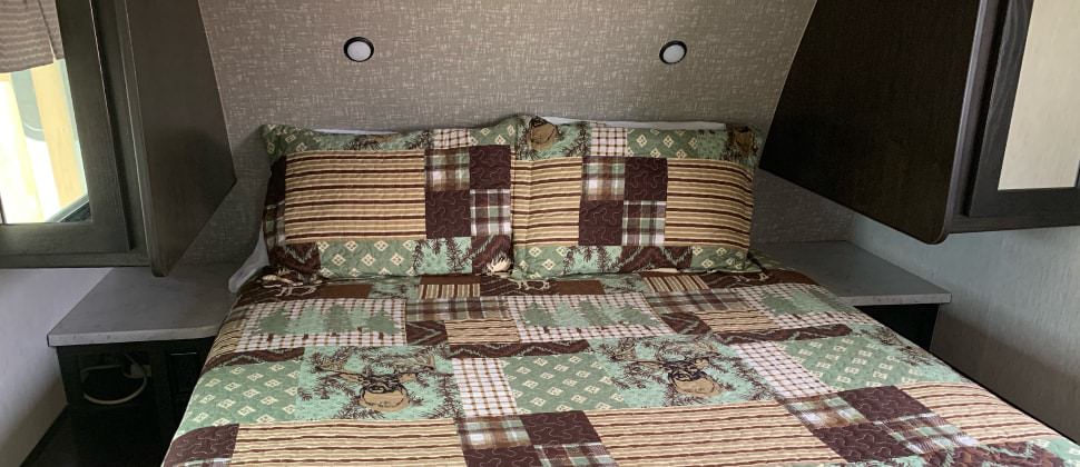 Bedroom in camper with dark wooden cabinets and sage, brown, and cream patchwork quilt bedding