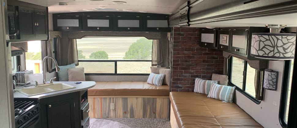 View of kitchen in camper with stainless steel refrigerator, black stove and microwave, dark wooden cabinets, and leather furniture